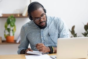 Student with headphones taking notes from the laptop